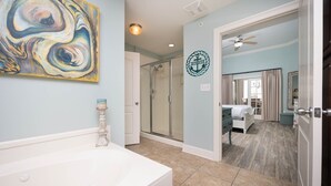 A bathroom with a bathtub, a glass shower enclosure, and a wall with a nautical-themed logo. - The Oasis 3003 Formerly Phoenix West Ii 3003 3 Bedroom Condo (Orange Beach)