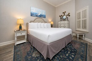 A neatly arranged bedroom with a large bed, two bedside tables with lamps, a dresser, a decorative mirror, and a window with shutters. - The Oasis 3003 Formerly Phoenix West Ii 3003 3 Bedroom Condo (Orange Beach)