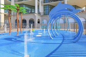A water play area with a pool, a blue spiral slide, and palm trees. - The Oasis 503 Formerly Phoenix West Ii 503 3 Bedroom Condo (Orange Beach)