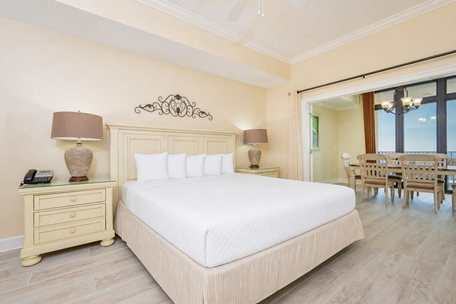Une chambre d’hôtel avec un grand lit, deux tables de chevet avec des lampes, un coin repas avec une table et des chaises, et une vue à travers une porte vitrée.