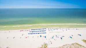 A beach with rows of sunbeds and umbrellas, a clear sky, and calm sea. - The Oasis 2608 Formerly Phoenix West Ii 2608 3 Bedroom Condo (Orange Beach)