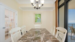 A dining room with a marble table, white chairs, a chandelier, and a painting on the wall. - The Oasis 2608 Formerly Phoenix West Ii 2608 3 Bedroom Condo (Orange Beach)