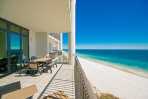 A balcony with a view of a beach, outdoor furniture, and a clear sky. - The Oasis 1205 Formerly Phoenix West Ii 1205 3 Bedroom Condo (Orange Beach)