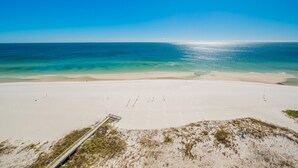 Una spiaggia con cielo sereno, una battigia sabbiosa e una passeggiata che conduce all'acqua.