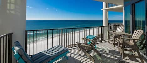 A balcony with a view of the beach, furnished with chairs and a table.