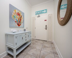Ein Flur mit einem weißen Schrank, einem farbenfrohen abstrakten Gemälde, einem Strandhinweisschild und einem Spiegel an der Wand.