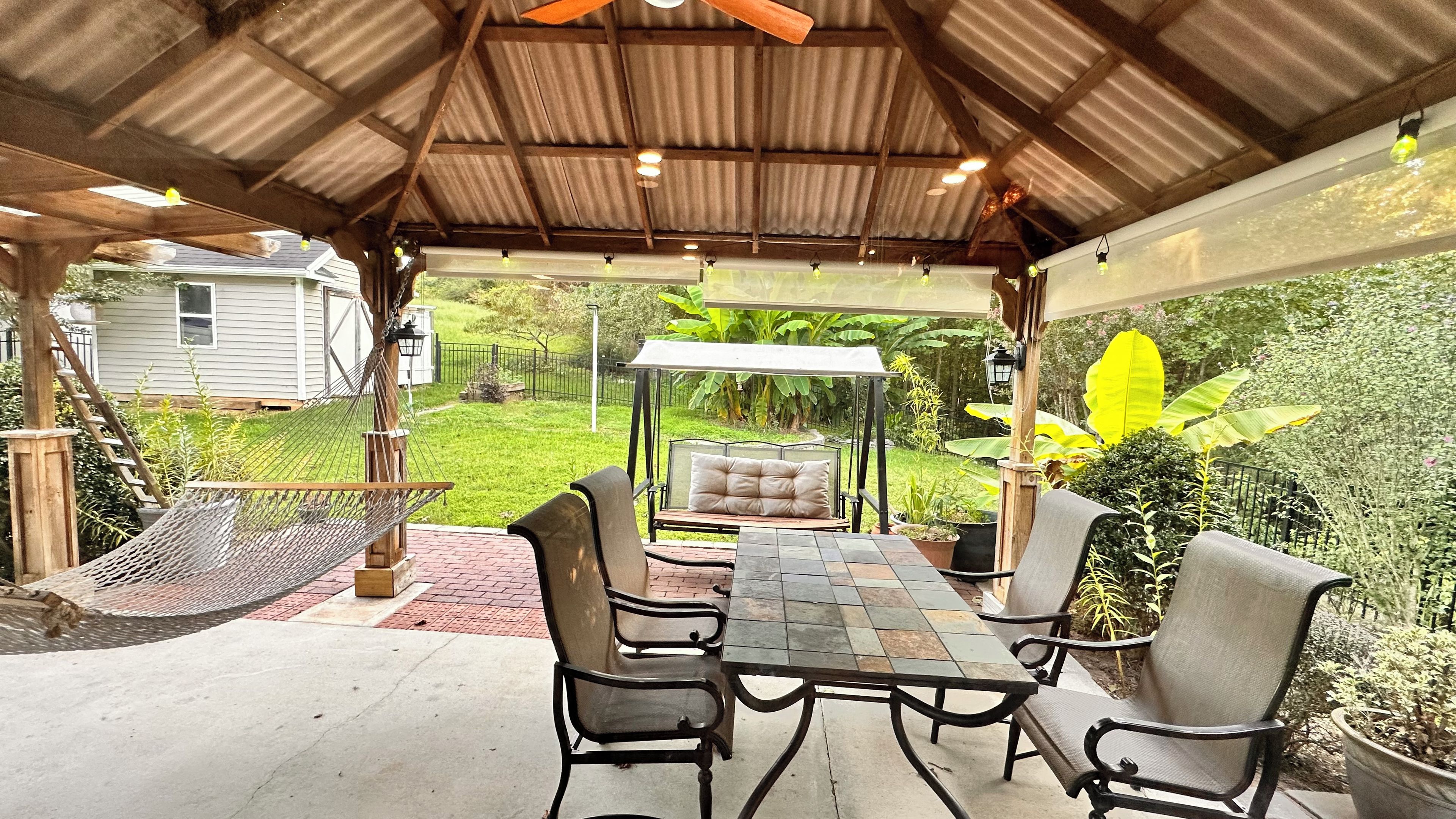 Une terrasse extérieure avec une table et des chaises, un hamac et un espace salon couvert donnant sur le jardin.