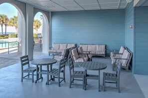 A covered outdoor seating area with tables and chairs, a pool, and a view of the ocean. - The Oasis 2402 Formerly Phoenix West Ii 2402 3 Bedroom Condo (Orange Beach)