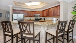 A kitchen with a central island, wooden cabinets, and a stainless steel refrigerator. - The Oasis 2402 Formerly Phoenix West Ii 2402 3 Bedroom Condo (Orange Beach)