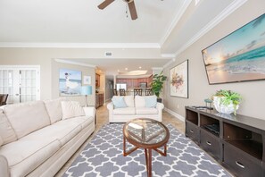 A spacious living room with a sofa, a glass coffee table, and a TV mounted on the wall. - The Oasis 2402 Formerly Phoenix West Ii 2402 3 Bedroom Condo (Orange Beach)