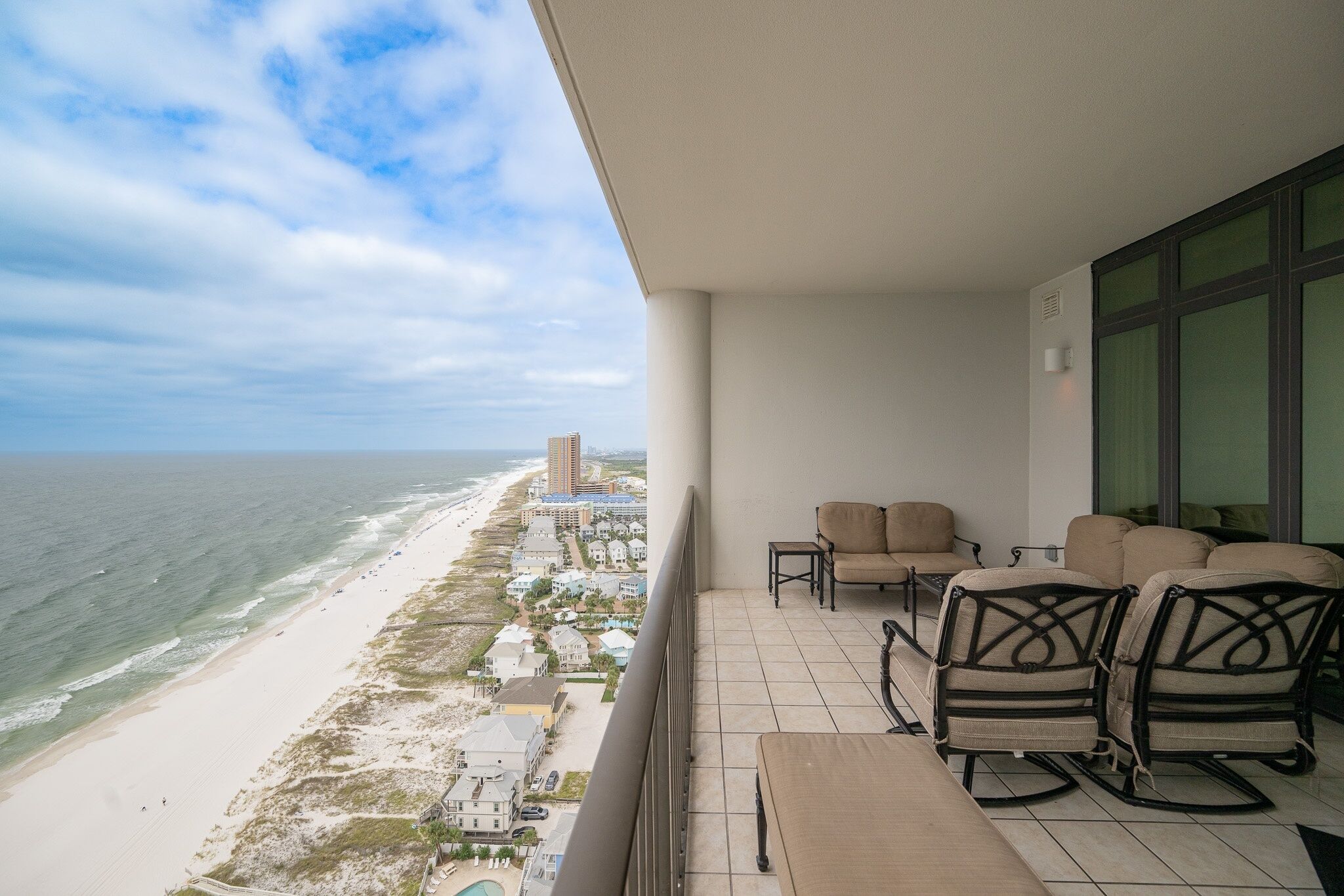 A balcony with a view of the beach and ocean, furnished with chairs and a table.