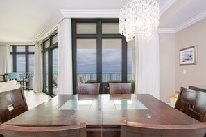 A dining area with a large table, chairs, and a view of the ocean through large windows. - The Oasis 2402 Formerly Phoenix West Ii 2402 3 Bedroom Condo (Orange Beach)