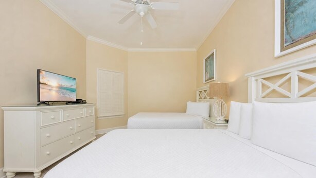 A hotel room with a bed, a dresser, a television, a ceiling fan, and a painting on the wall. - The Oasis 2609 Formerly Phoenix West Ii 2609 3 Bedroom Condo (Orange Beach)