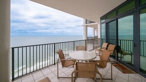 A balcony with a view of the sea, a round table with chairs, and a glass door. - The Oasis 2609 Formerly Phoenix West Ii 2609 3 Bedroom Condo (Orange Beach)