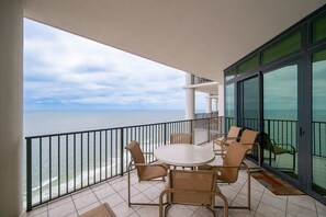 Ein Balkon mit Meerblick, ein runder Tisch mit Stühlen und eine Glastür.
