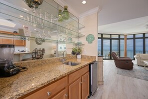 A modern kitchen with granite countertops, a built-in dishwasher, and a glass wine rack. - The Oasis 2609 Formerly Phoenix West Ii 2609 3 Bedroom Condo (Orange Beach)