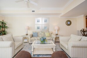 A living room with a sofa set, two side tables, a coffee table, a ceiling fan, and a wall clock. - The Oasis 2609 Formerly Phoenix West Ii 2609 3 Bedroom Condo (Orange Beach)