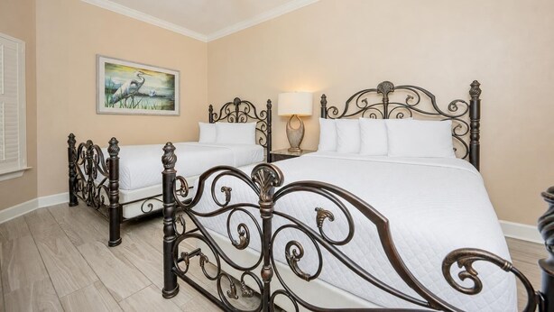 A bedroom with two beds, a ceiling fan, a painting, and a nightstand with a lamp. - The Oasis 2306 Formerly Phoenix West Ii 2306 3 Bedroom Condo (Orange Beach)