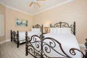 A bedroom with two beds, a ceiling fan, a painting, and a nightstand with a lamp. - The Oasis 2306 Formerly Phoenix West Ii 2306 3 Bedroom Condo (Orange Beach)