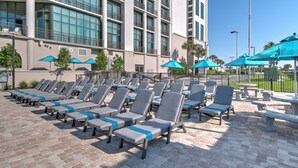 A rooftop pool area with sun loungers and umbrellas, a high-rise building in the background, and a clear sky. - The Oasis 2306 Formerly Phoenix West Ii 2306 3 Bedroom Condo (Orange Beach)
