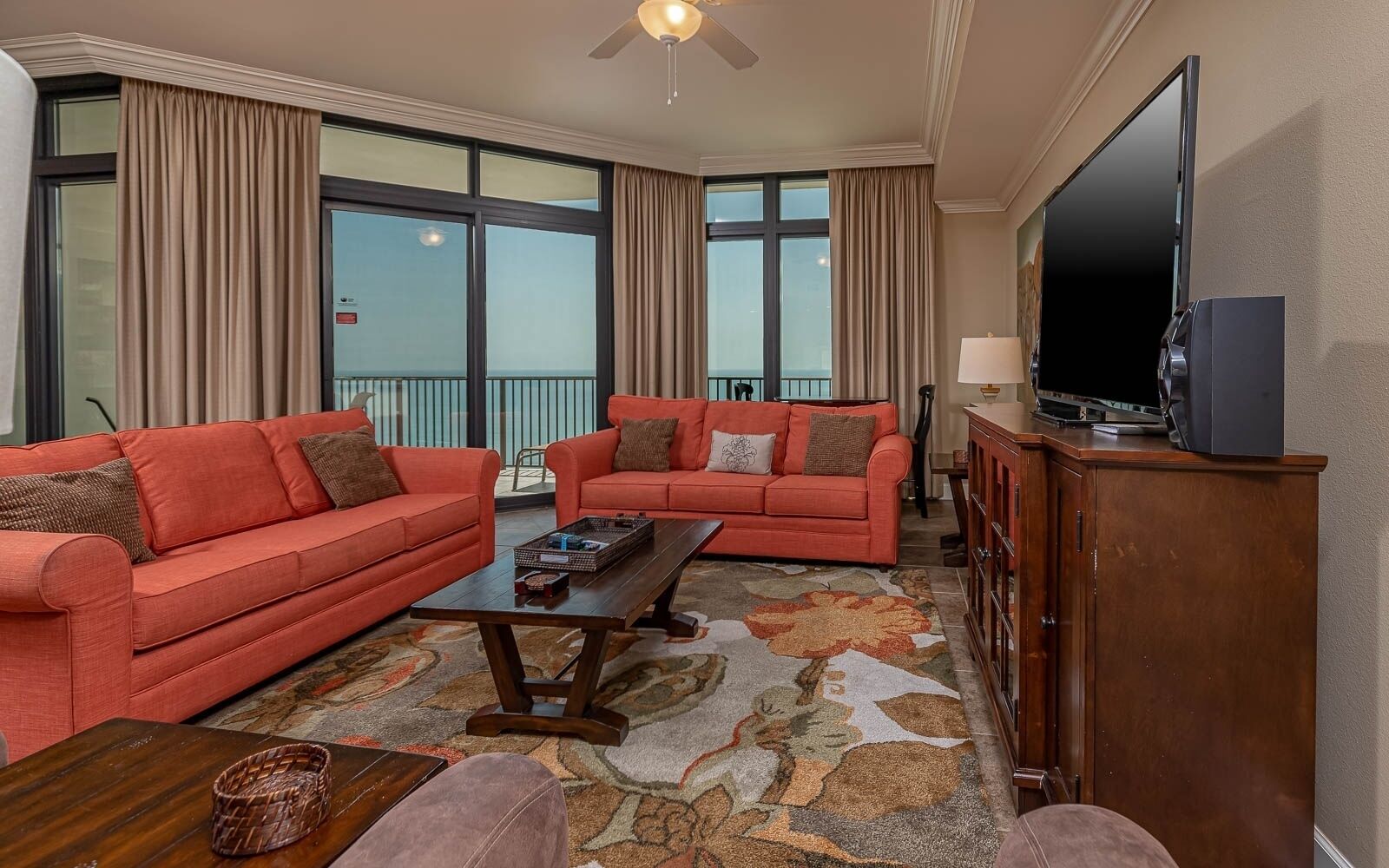 A living room with two red sofas, a coffee table, a television on a cabinet, and a balcony with curtains.