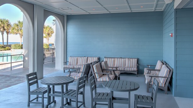 A covered outdoor seating area with tables and chairs, a pool, and a view of the ocean. - The Oasis 3006 Formerly Phoenix West Ii 3006 3 Bedroom Condo (Orange Beach)