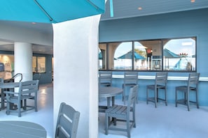 Um restaurante com mesas ao ar livre, uma janela grande e um toldo azul.