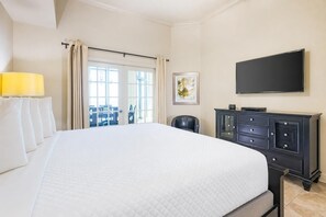 A hotel room with a large bed, a flat-screen TV, a dark wooden dresser, and a view through a glass door. - The Oasis 3208 Formerly Phoenix West Ii 3208 3 Bedroom Condo (Orange Beach)