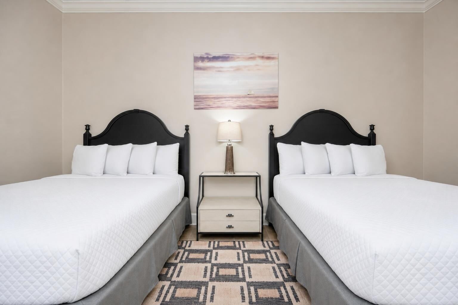 A hotel room with two beds, a nightstand, a lamp, and a painting on the wall.