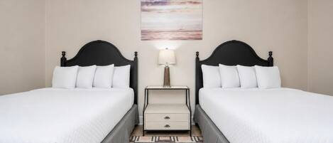 A hotel room with two beds, a nightstand, a lamp, and a painting on the wall.