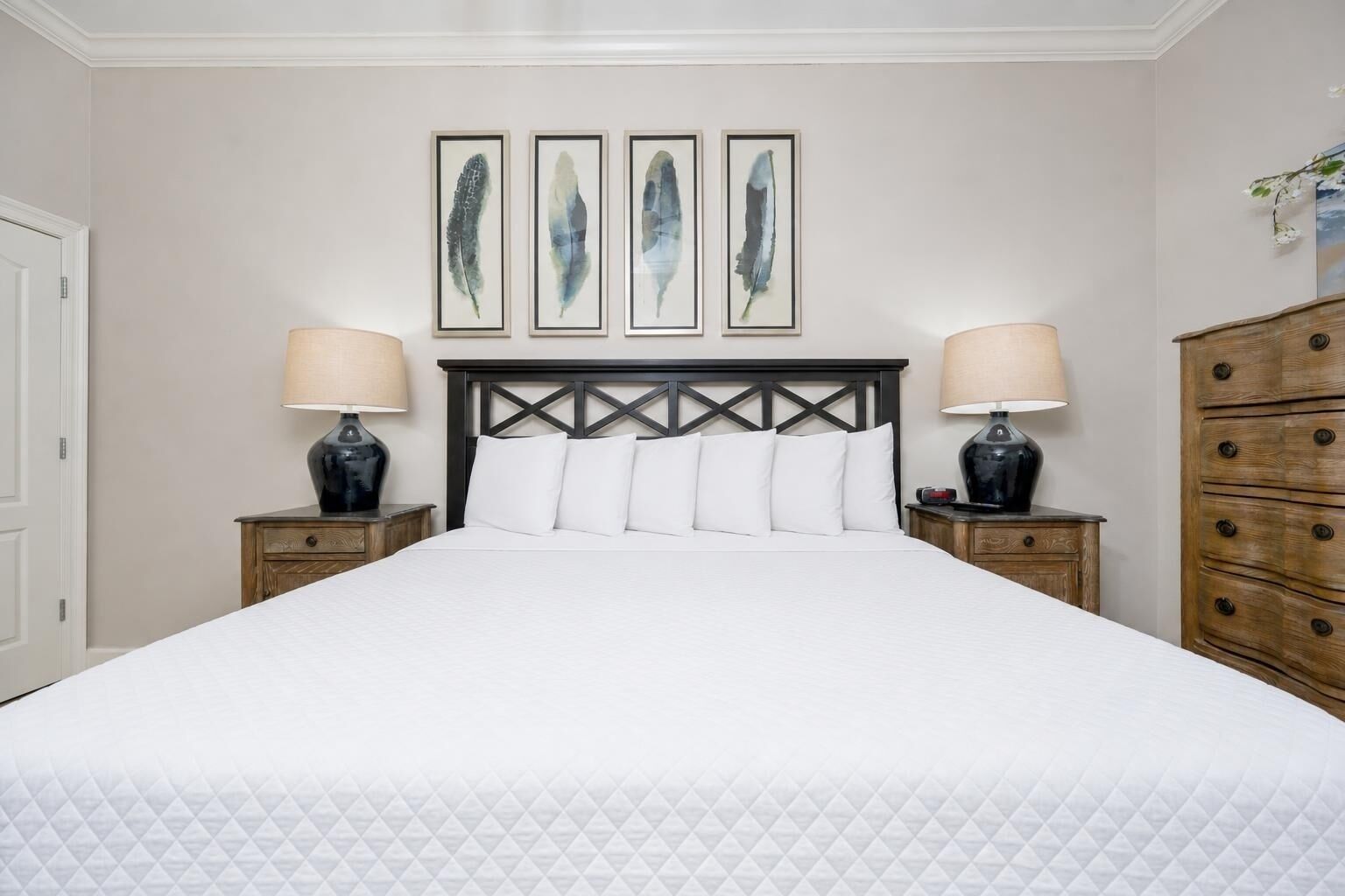 A hotel room with a large bed, two bedside tables with lamps, a wooden dresser, and four framed wall art pieces.