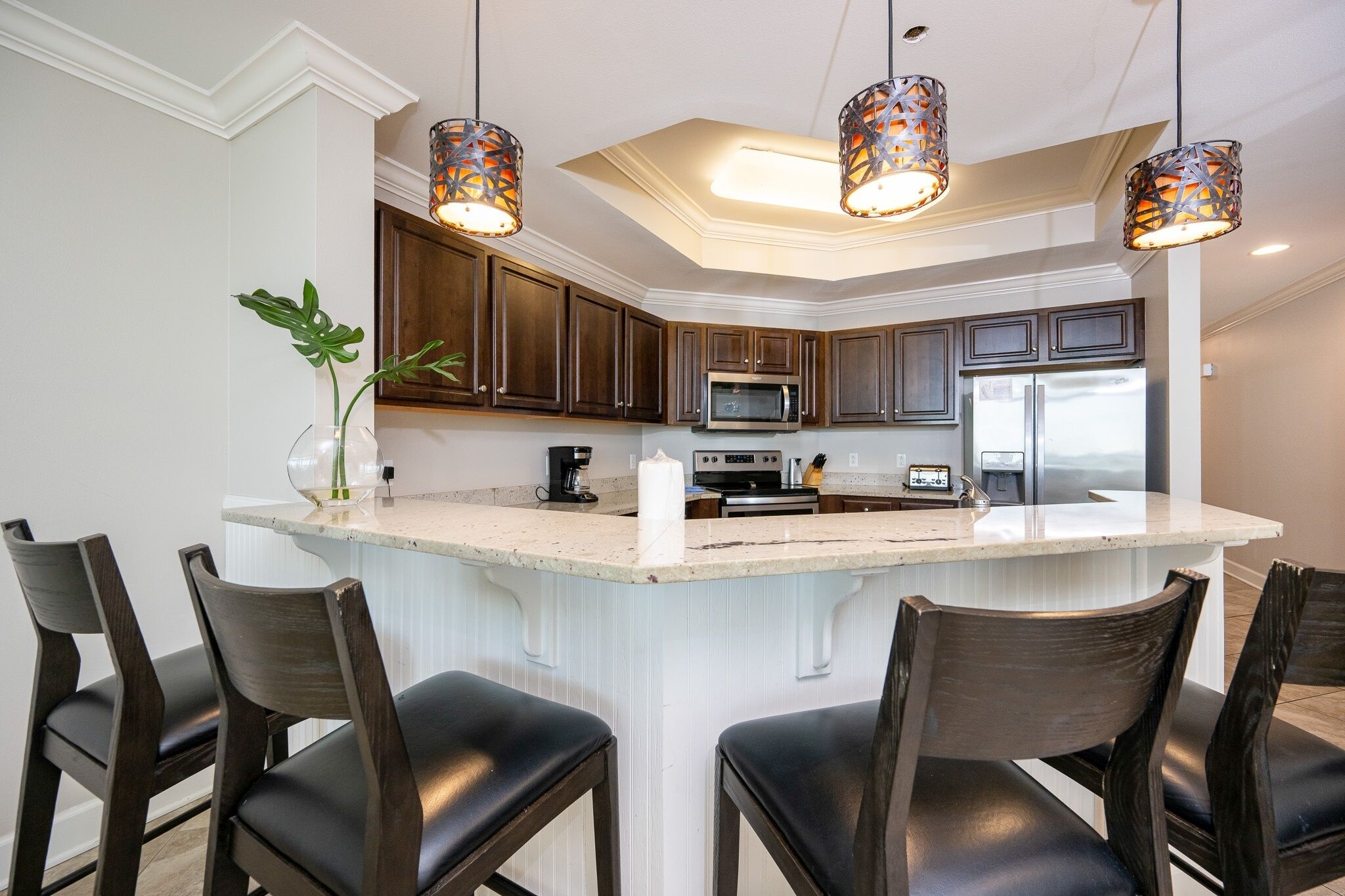 A modern kitchen with dark wooden cabinets, a central island with bar stools, stainless steel appliances, and pendant lighting.