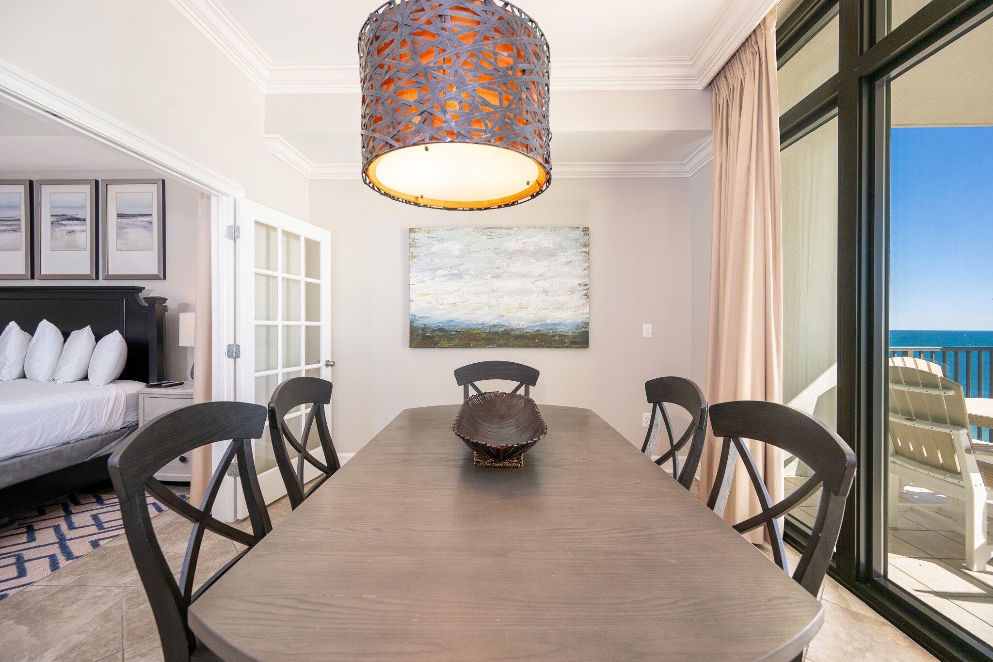 Habitación de hotel con una mesa de comedor, sillas, una cama, un cuadro y vista al océano.