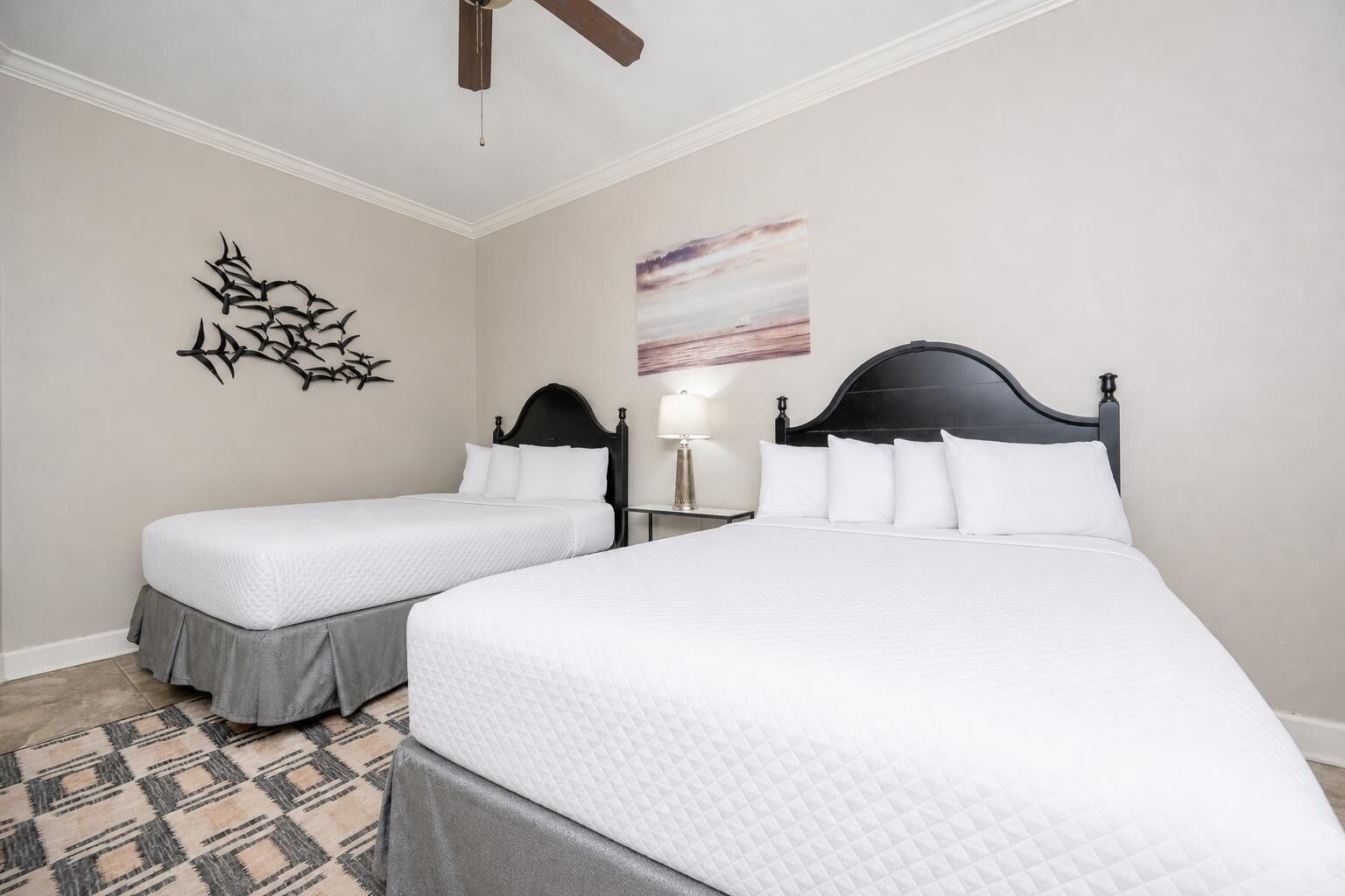 Habitación de hotel con dos camas, ventilador de techo, una obra de arte en la pared y alfombra estampada.