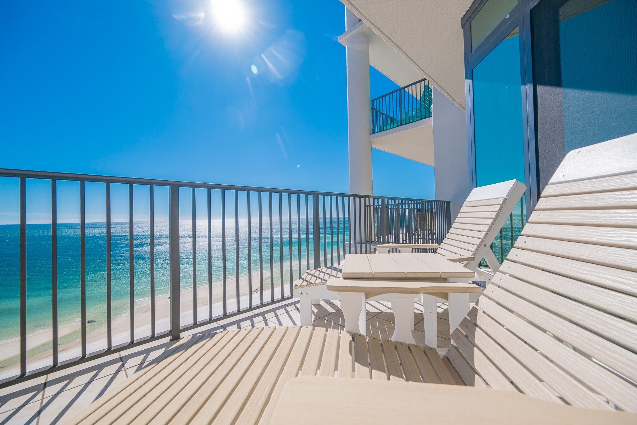 A balcony with a view of the ocean, a table, and two lounge chairs.