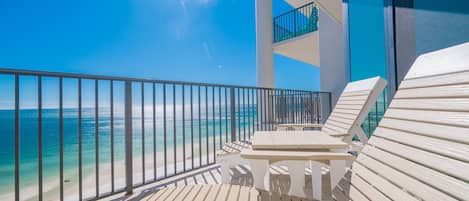 A balcony with a view of the ocean, a table, and two lounge chairs.