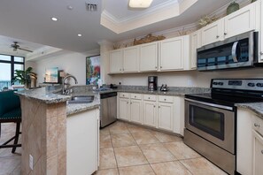 A modern kitchen with granite countertops, stainless steel appliances, and a large island with a sink. - The Oasis 404 Formerly Phoenix West Ii 404 3 Bedroom Condo (Orange Beach)