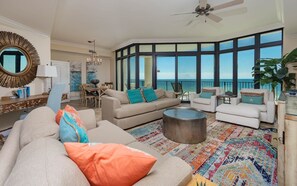 A spacious living room with a large window overlooking the ocean, a ceiling fan, and a variety of seating options. - The Oasis 404 Formerly Phoenix West Ii 404 3 Bedroom Condo (Orange Beach)