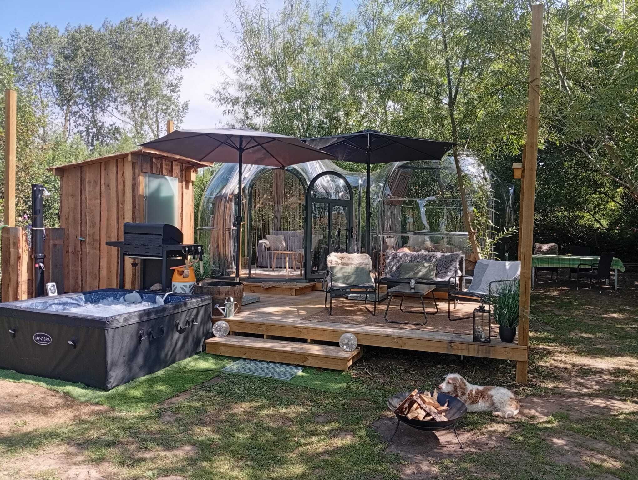 Una cabaña de madera con un jacuzzi, un porche cubierto con mobiliario exterior y un invernadero de vidrio.