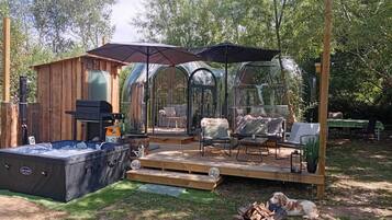 Una cabaña de madera con un jacuzzi, un porche cubierto con mobiliario exterior y un invernadero de vidrio.