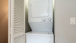 Uma lavanderia compacta e branca, com máquina de lavar e secar de abertura frontal, um pequeno painel de controle com configurações de temperatura e tamanho de carga, e uma porta com puxador.