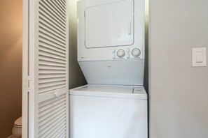 A compact, white laundry room with a front-loading washer and dryer, a small control panel with temperature and load size settings, and a door with a handle. - Sunset Vista 3 Bedroom Condo (Telluride)