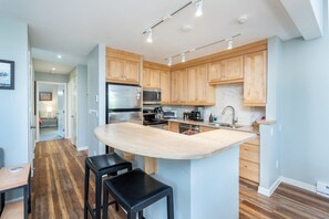 A modern kitchen with wooden cabinets, stainless steel appliances, and a central island with bar stools. - Sunset Vista 3 Bedroom Condo (Telluride)