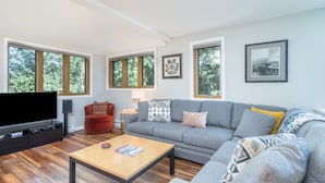 Uma sala de estar moderna com um sofá cinzento, uma poltrona vermelha, uma mesa de centro de madeira e uma televisão de tela plana.
