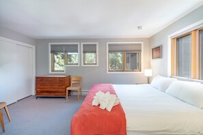 Ein Schlafzimmer mit Bett, Schminktisch, Stuhl und zwei Fenstern mit Jalousien.