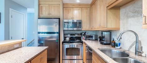 A modern kitchen with wooden cabinets, stainless steel appliances, granite countertops, and a double sink.