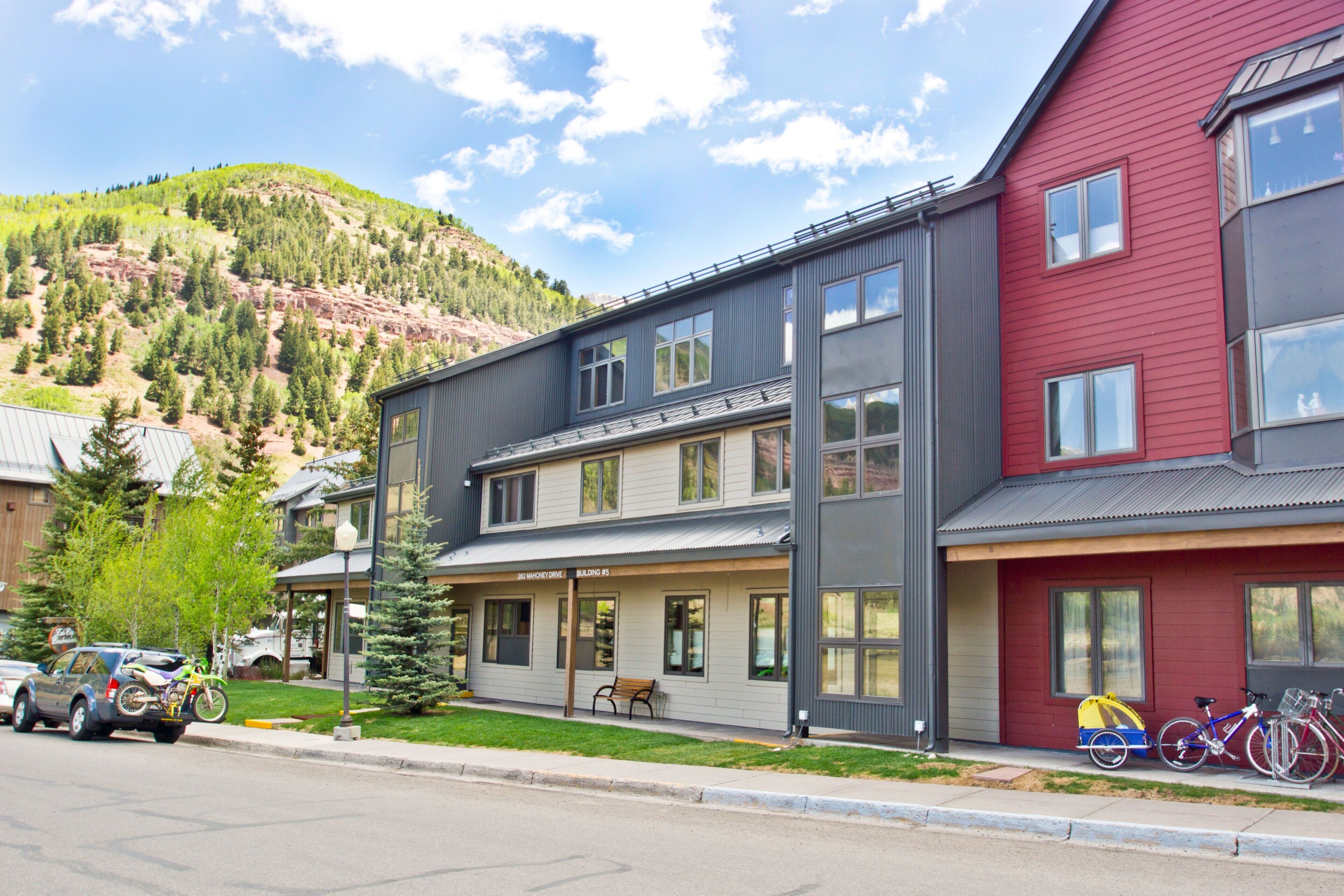 A multi-story building with a covered porch and a mountain backdrop.