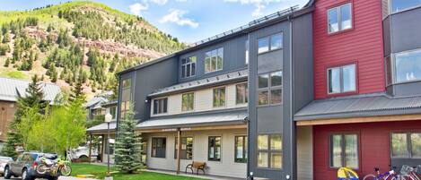 A multi-story building with a covered porch and a mountain backdrop.