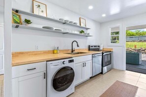A modern kitchen with white cabinetry, a wooden countertop, a built-in washing machine, and a window providing a view of the outdoors. - Big Island Kahaluu Surf Boutique #4 2 Bedroom Apts (Kailua-Kona)