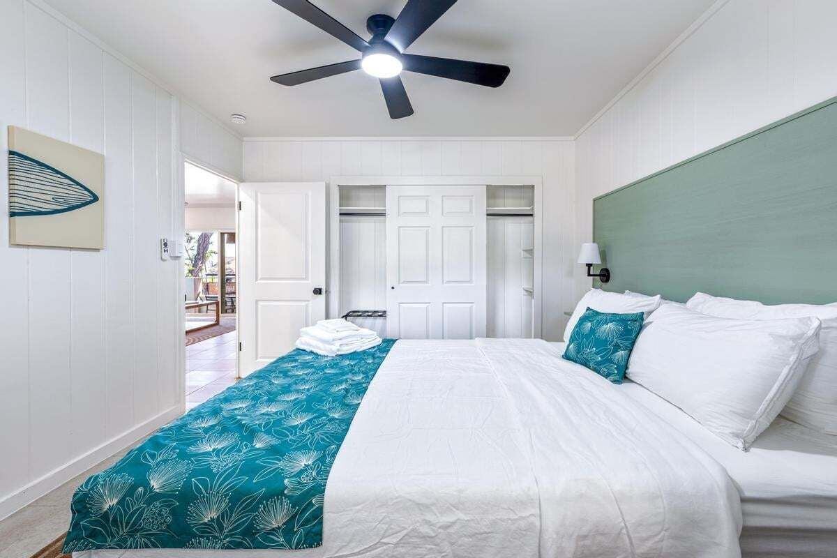 Une chambre à coucher avec un lit, un ventilateur de plafond, une tête de lit verte et une porte blanche.